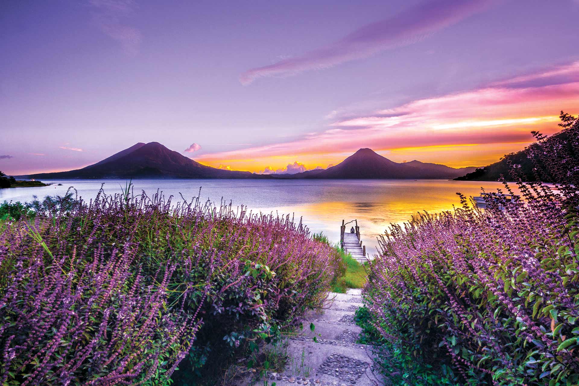 A view of a lake from a field during a beautiful orange and purple sunset