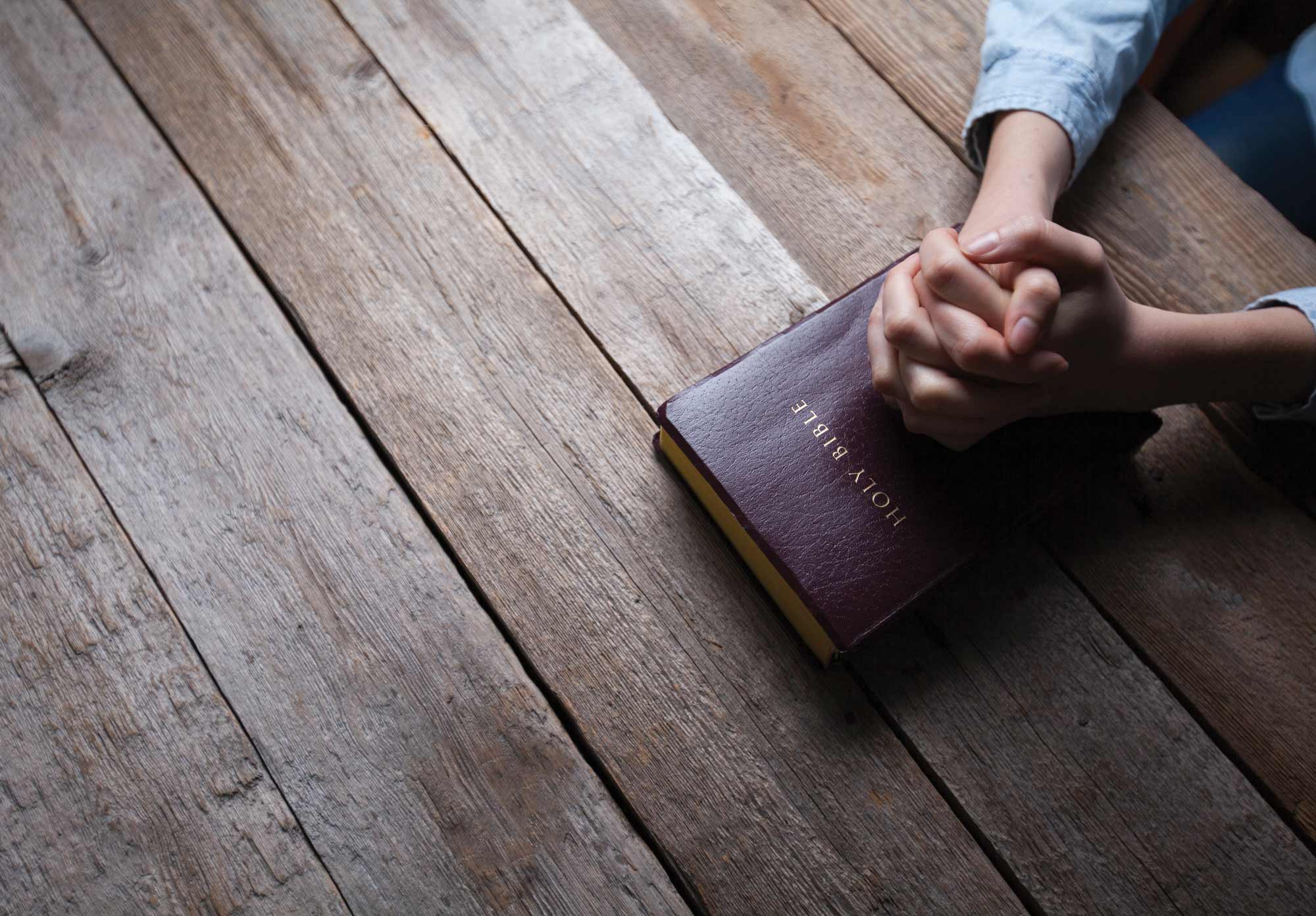 Hands clasped in prayer on top of a Bible