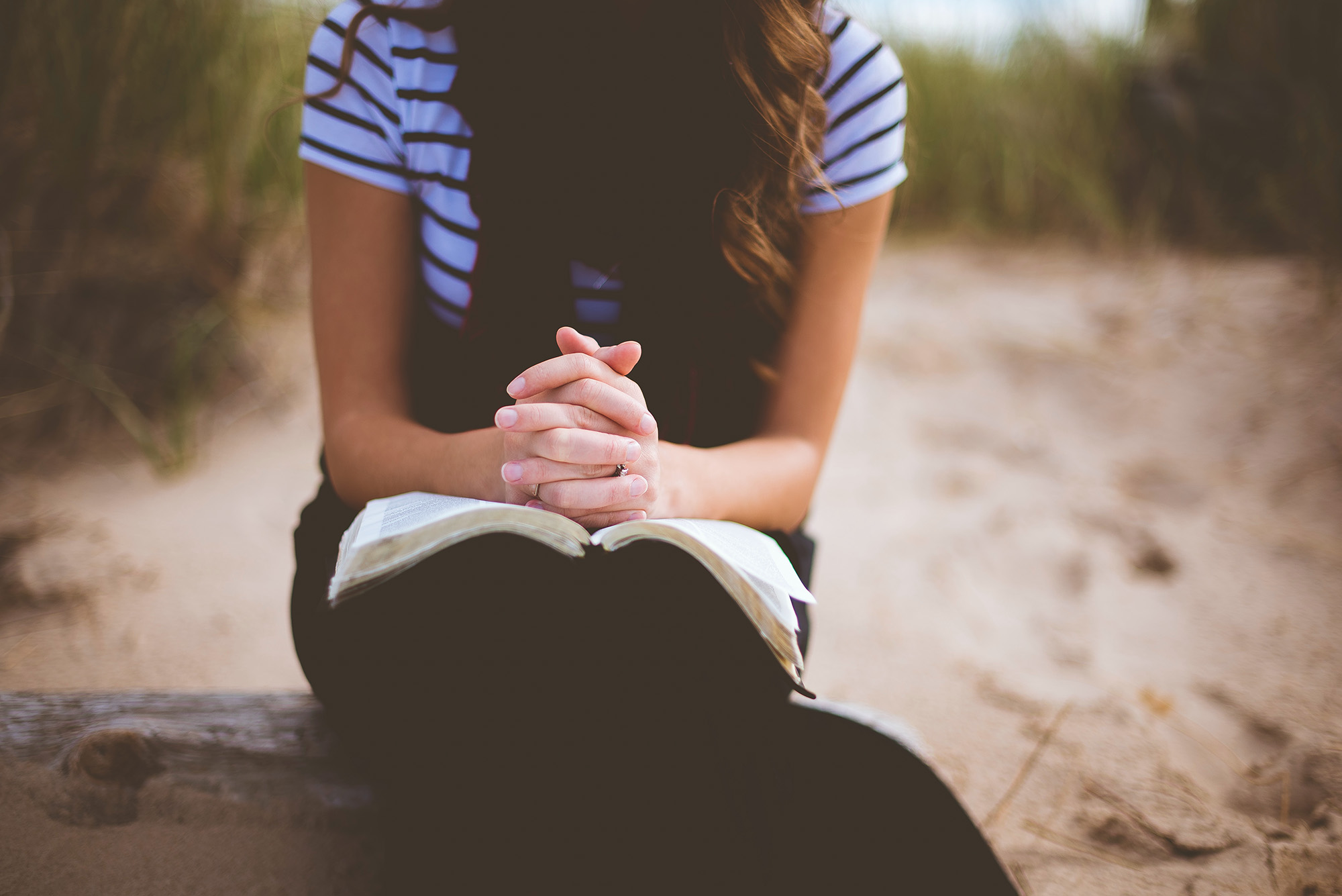 A woman prayers on the beach while reading a Bible